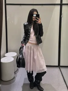Schicke schwarze Lederjacke kombiniert mit rosa Plisseerock und Stiefeln für stilvolle Damen.
