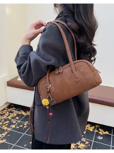 Brown vintage shoulder pillow bag with contrast stitching and charming pendant detail.