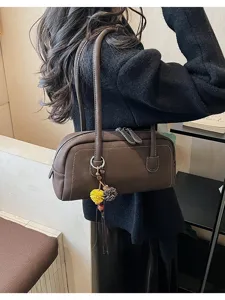 Detail shot of the stylish brown shoulder pillow bag with plush charm in daily scene.