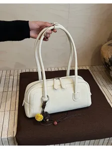 Detailed view of white leather shoulder pillow bag with double straps and cute flower charm.