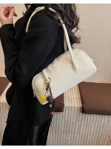 Detail view of minimalist beige shoulder pillow bag for women, retro casual handbag with charms.