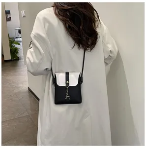 Close up detail showing the black and white mini crossbody phone bag worn by a model indoors.