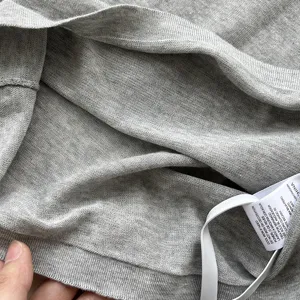 Détail du tissu du top en tricot gris montrant texture douce et étiquette, haute qualité.