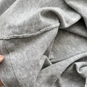 Détail haut pull en tricot gris montrant texture fine, tissu doux et coutures délicates.