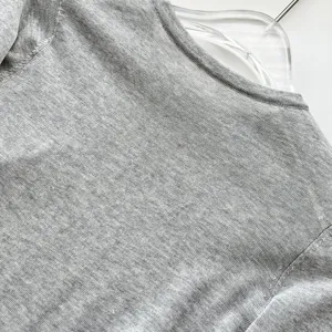Détail de tissu tricoté gris montrant une texture semi-transparente et un col rond délicat.