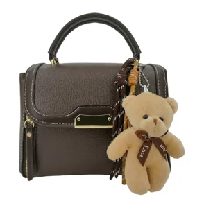 Brown leather handbag detail, metal clasp, decorative cute teddy bear pendant and woven cords.