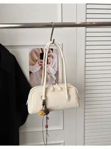 Close-up detail view of the cream white leather shoulder pillow bag with stylish hanging charm.
