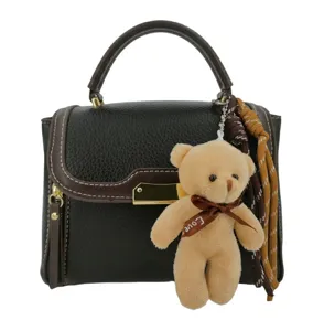 Detail shot of the dark brown leather handbag featuring a cute teddy bear charm and metal clasp.