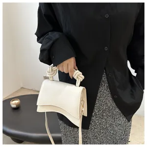 Minimalist white top-handle crossbody bag with unique knotted handle and curved flap design.