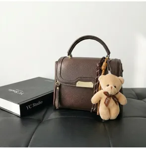 Brown leather top handle shoulder bag with cute bear pendant and stylish metal clasp.