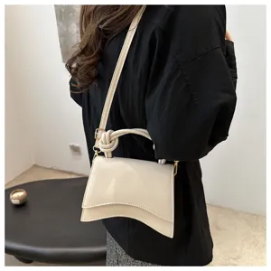 Detail shot of a stylish curved solid color handbag with chic knotted handle and shoulder strap.