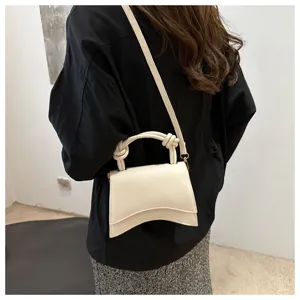 Detailed view of minimalist white leather crossbody handbag featuring unique curved base.