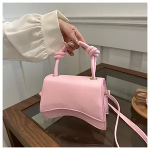 Pink leather handbag with unique curved bottom shape and twisted handle design detail.