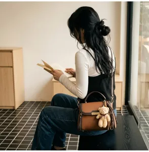 Stylish color-block shoulder bag with top handle, crossbody strap, and cute bear charm.
