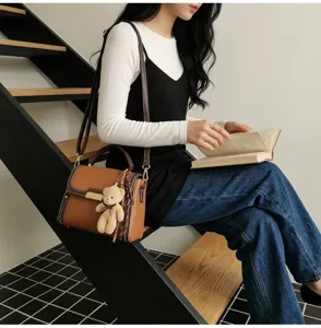 Detail view of stylish color-blocked women's shoulder bag with cute bear pendant and strap.