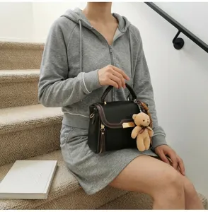 Detailed shot of stylish black leather handbag with brown trim, metal clasp and cute bear charm.