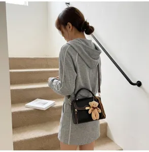 Detailed view of the stylish contrast color shoulder bag with cute bear pendant and top handle.