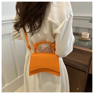 Orange handbag detail view showing curved flap design and chic shoulder strap style.