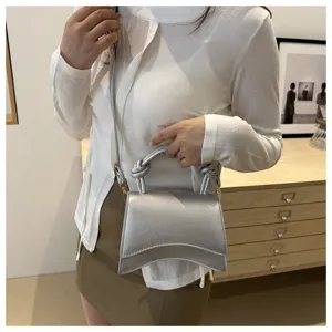 Detailed view of a trendy silver leather shoulder bag with unique curved design and top handle.