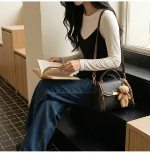 Detailed shot of dark leather crossbody bag with cute bear pendant in modern indoor setting.