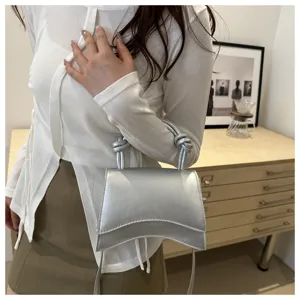 Silver leather detail view of the fashionable curved shoulder bag with top handle and strap.