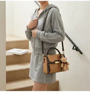 Fashionable contrast color women's shoulder bag with cute bear pendant and top handle.