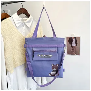 Lila Canvas Umhängetasche Detailansicht mit Vordertasche, Logo und niedlichem Bären-Druck.