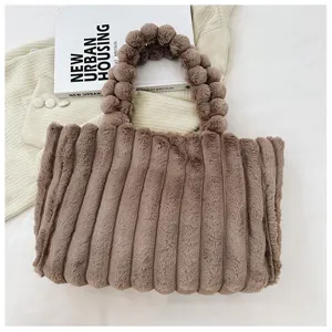 Detail shot of brown plush pleated tote bag with unique pom-pom handle texture and soft fabric.