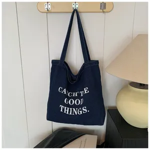 Detailed view of casual denim tote bag with letter print, hanging on wall with warm lamp.