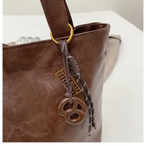 Brown PU leather tote bag close-up featuring texture, metal ring and decorative charm detail.