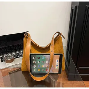Brown suede hobo shoulder bag detail showing soft slouchy design and wide strap on table.