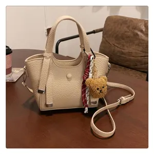 Beige leather tote bag for women, stylish crossbody shoulder bag with cute bear charm.