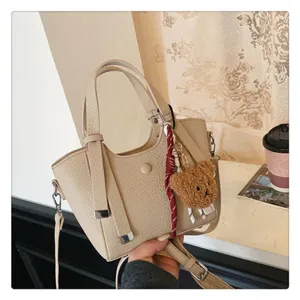 Detail view of the stylish beige leather tote bag, featuring a cute plush bear pendant.