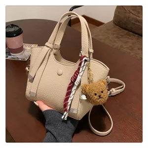 Detailed view of a stylish beige tote bag with a cute plush bear pendant and chic woven rope.