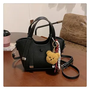 Detailed view of black leather tote bag with cute bear keychain and stylish ribbon decoration.