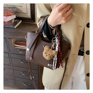 Detail view of brown leather tote bag handle and cute bear charm pendant for autumn.