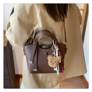 Detail shot of brown leather shoulder tote bag featuring cute plush bear charm and ribbon.