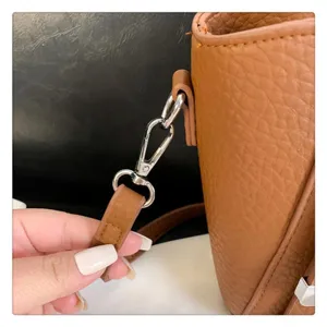 Close-up detail shot of brown leather tote bag strap hardware and durable metal hook.