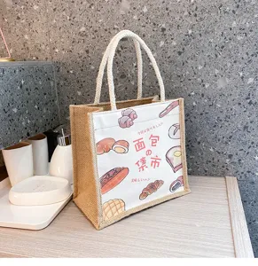 Detailansicht der Jute-Leinwand-Tasche mit süßem Brot-Druck und geflochtenen Griffen auf Theke.