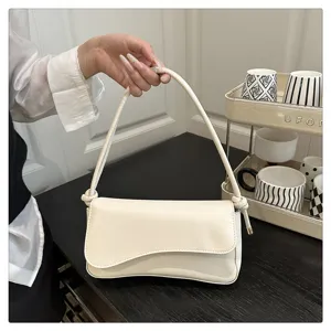 Details of the creamy white minimalist shoulder bag with unique flap and delicate knot strap.