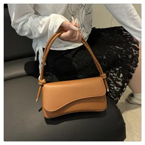 Brown underarm shoulder bag for women, stylish niche design handbag with unique flap and knots.