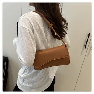 Detail shot of minimalist brown underarm shoulder bag worn on shoulder, elegant daily accessory.