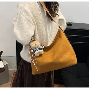 Detailed view of brown suede hobo shoulder bag with charming bear pendant in casual setting.