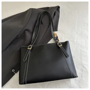 Black commuter tote bag detail shot, featuring white contrast stitching, golden hardware, and chic scarf.