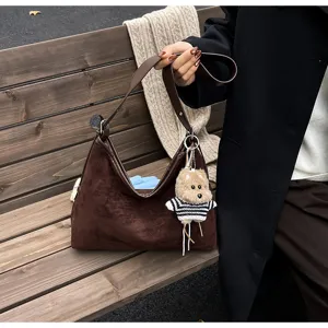 Detailed view of the vintage brown suede slouchy shoulder bag with cute plush keychain on bench.