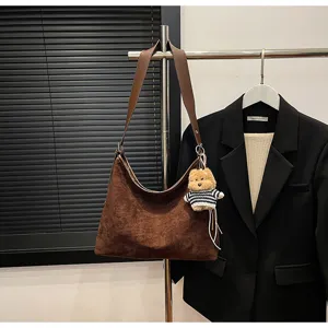 Detailed view of the brown suede slouchy shoulder bag with cute bear pendant on rack.