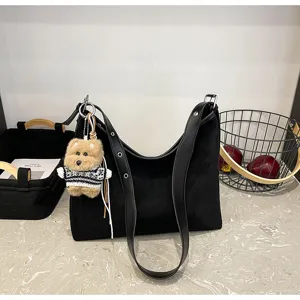 Detailed view of black suede shoulder bag with cute bear plush pendant and wide strap.