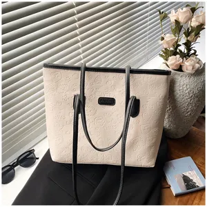 Detailed view of large capacity beige tote bag with debossed pattern and chic black handles.