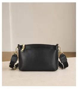 Detailed view of the black leather crossbody handbag highlighting gold zipper and strap design.