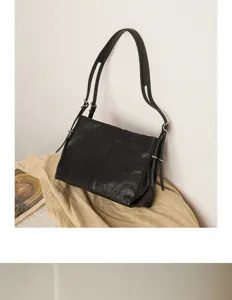 Detailed view of minimalist black leather shoulder bag with adjustable straps and metal rings.
